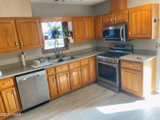 kitchen featuring brown cabinetry, stainless steel appliances, a sink, and light countertops