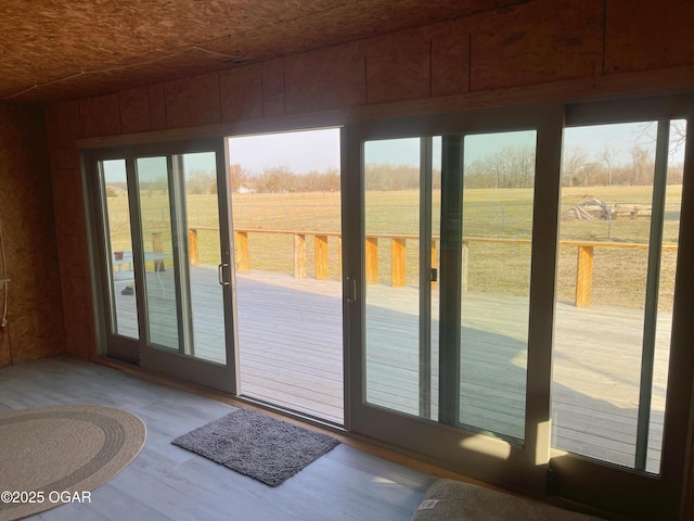 doorway to outside with a rural view, wood finished floors, and wooden walls