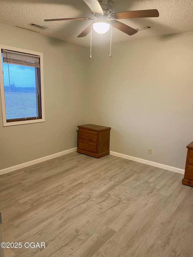 empty room with visible vents, a ceiling fan, a textured ceiling, wood finished floors, and baseboards