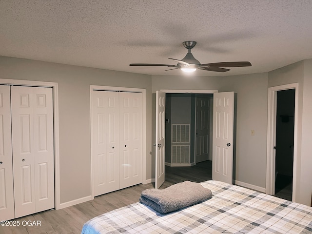 bedroom with a textured ceiling, wood finished floors, two closets, and baseboards