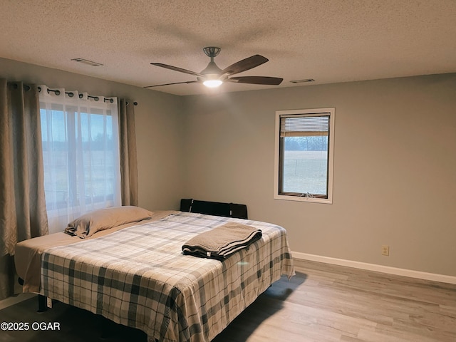 bedroom featuring visible vents, a textured ceiling, baseboards, and wood finished floors