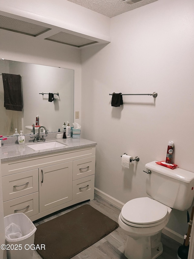 bathroom featuring baseboards, toilet, wood finished floors, a textured ceiling, and vanity