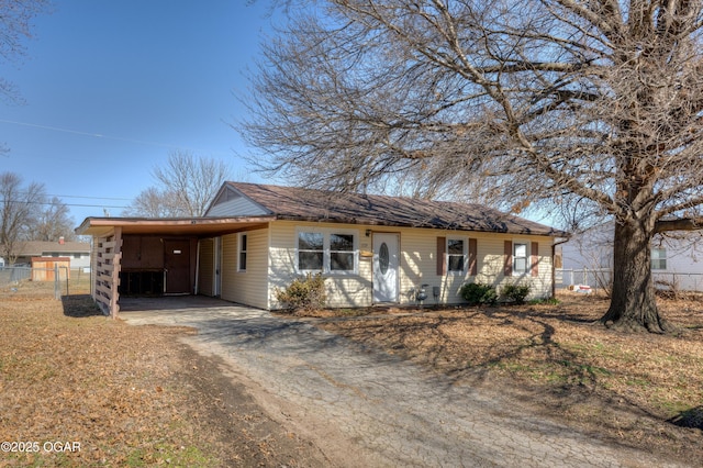 single story home featuring dirt driveway, an attached carport, roof with shingles, and fence