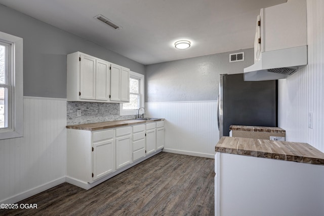 kitchen with wainscoting, butcher block counters, visible vents, and freestanding refrigerator