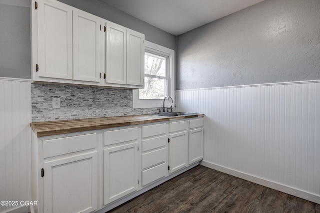 kitchen with butcher block countertops, a wainscoted wall, a sink, and white cabinetry