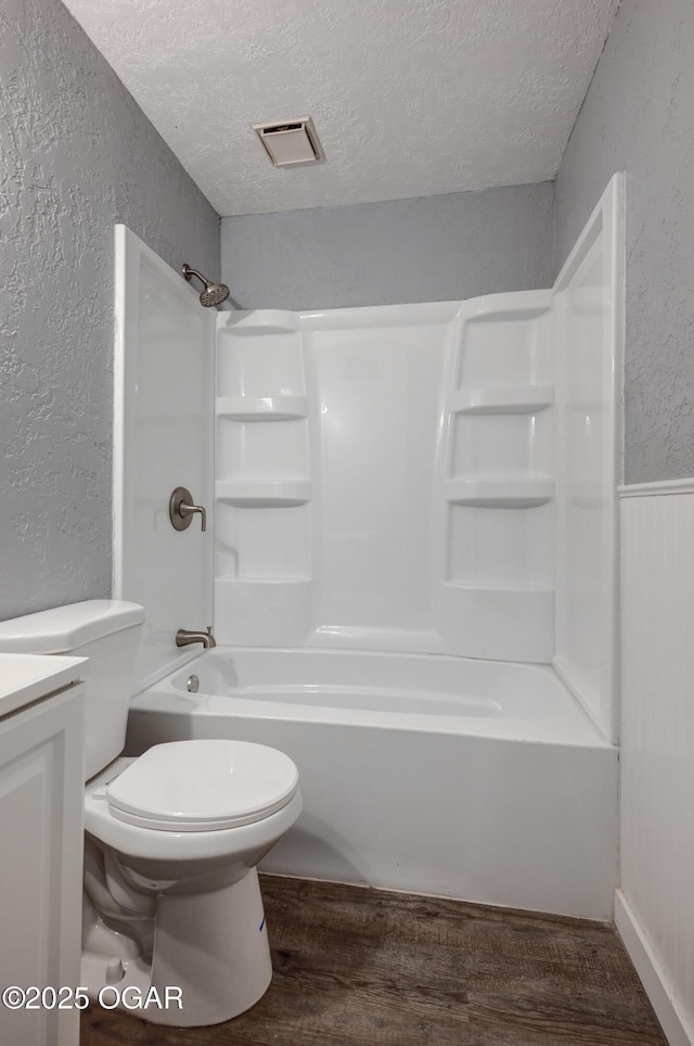 full bath featuring a textured ceiling, a textured wall, toilet, wood finished floors, and visible vents