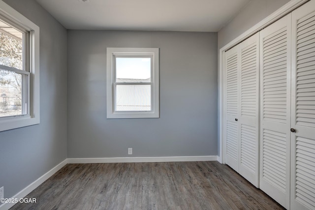 unfurnished bedroom with baseboards, dark wood-style flooring, and a closet