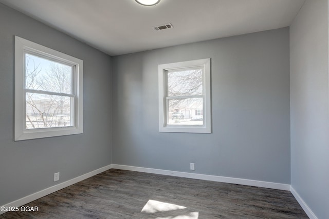 unfurnished room featuring dark wood finished floors, visible vents, and baseboards