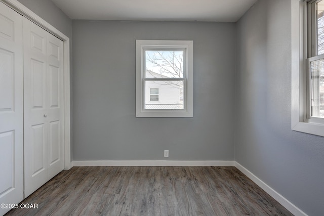 unfurnished bedroom with wood finished floors, multiple windows, a closet, and baseboards