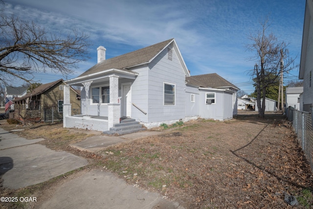 view of side of home featuring a shingled roof, a chimney, fence, and a porch