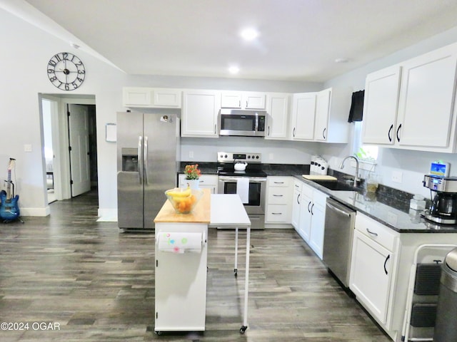 kitchen with dark countertops, appliances with stainless steel finishes, dark wood-style flooring, white cabinetry, and a sink