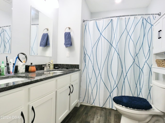 full bath featuring toilet, double vanity, a sink, and wood finished floors