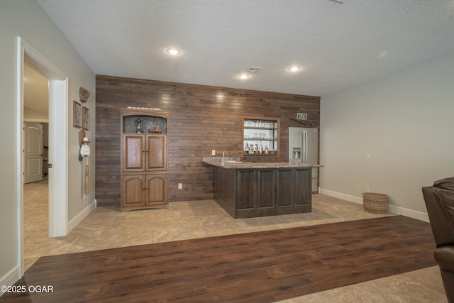 kitchen featuring light wood-type flooring, stainless steel fridge, wooden walls, and a peninsula