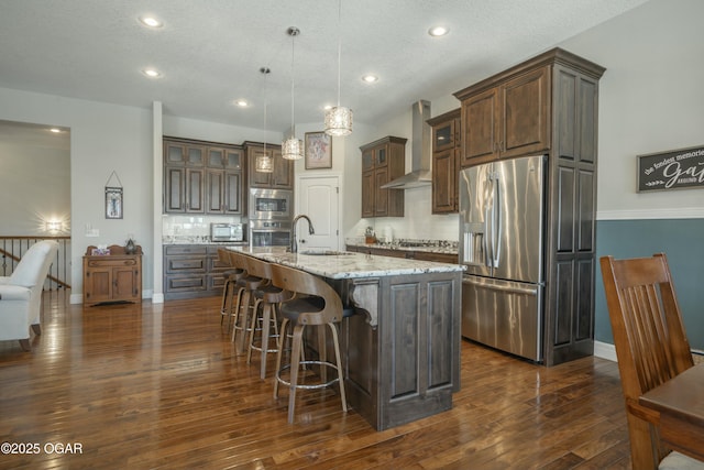 kitchen with a sink, dark wood-style floors, stainless steel appliances, wall chimney range hood, and decorative backsplash