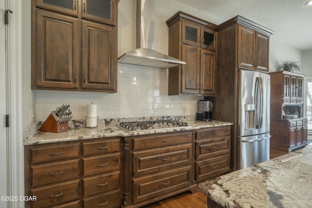 kitchen featuring tasteful backsplash, appliances with stainless steel finishes, wall chimney exhaust hood, and light stone counters