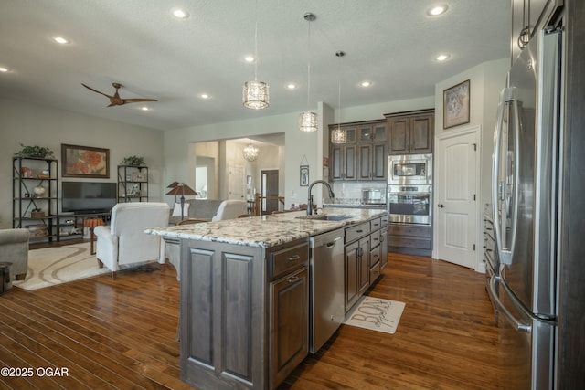 kitchen featuring dark brown cabinets, dark wood-type flooring, open floor plan, appliances with stainless steel finishes, and a sink