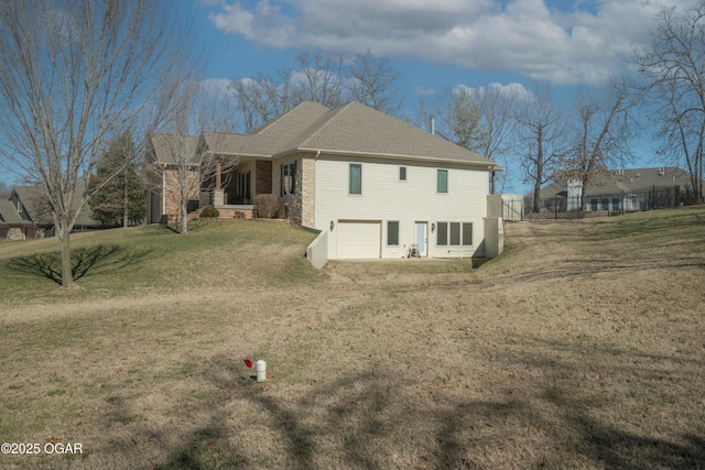 rear view of house with a lawn, stone siding, fence, a shingled roof, and a garage