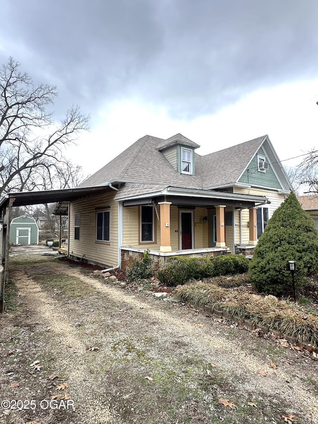 view of front of home with an outbuilding, a porch, an attached carport, driveway, and roof with shingles