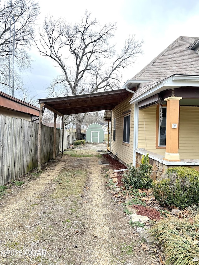 view of side of home with dirt driveway, a storage unit, fence, a carport, and an outdoor structure