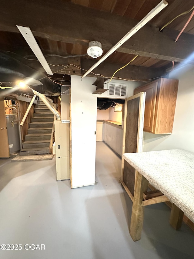 unfinished basement featuring water heater, stairs, and visible vents