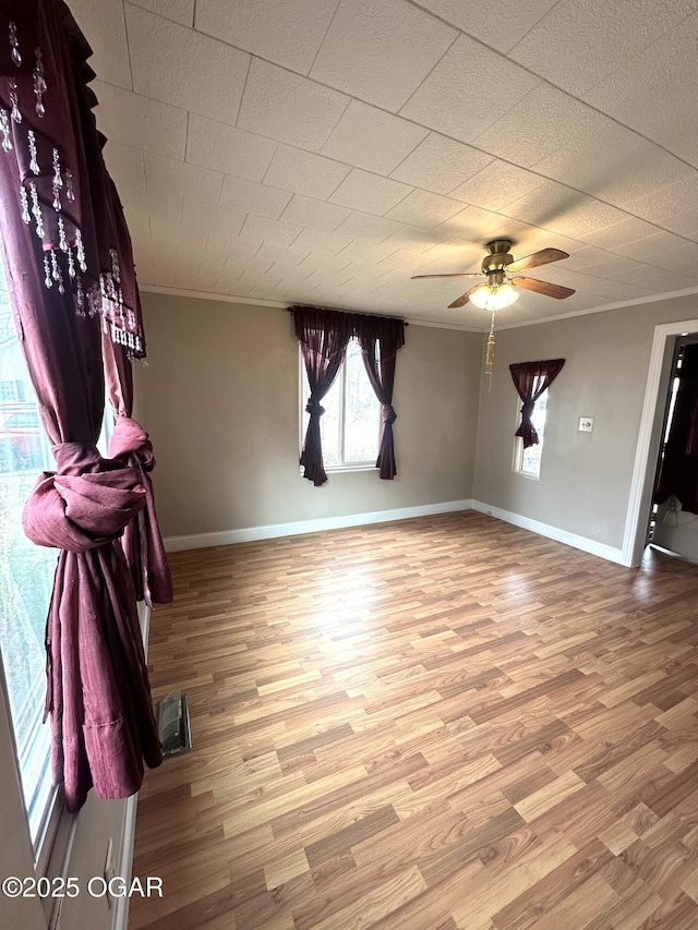 spare room featuring a ceiling fan, crown molding, baseboards, and wood finished floors