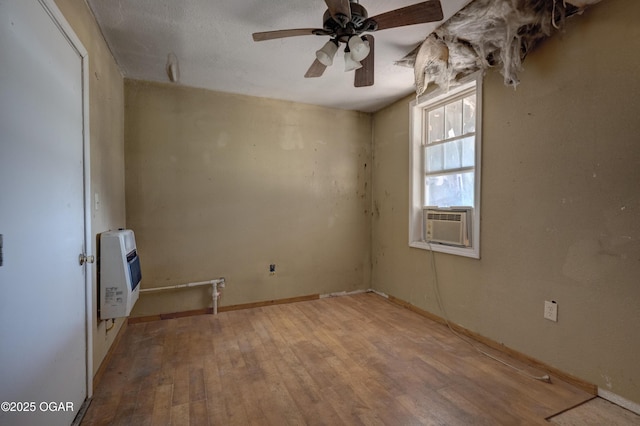 empty room with cooling unit, a ceiling fan, baseboards, heating unit, and wood-type flooring