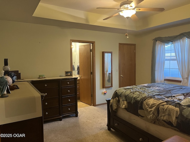 bedroom with light carpet, a tray ceiling, a ceiling fan, and baseboards