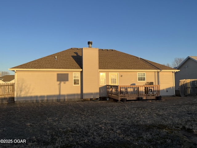 rear view of house with roof with shingles, a yard, a chimney, fence, and a deck