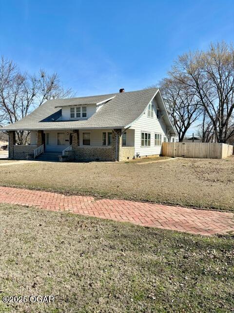 view of front of home featuring covered porch, a front lawn, and fence