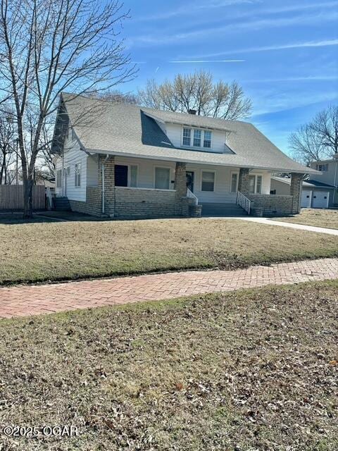 view of front of house featuring a porch, brick siding, fence, and a front lawn