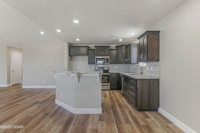 kitchen with light wood finished floors, a sink, decorative backsplash, stainless steel appliances, and a kitchen breakfast bar