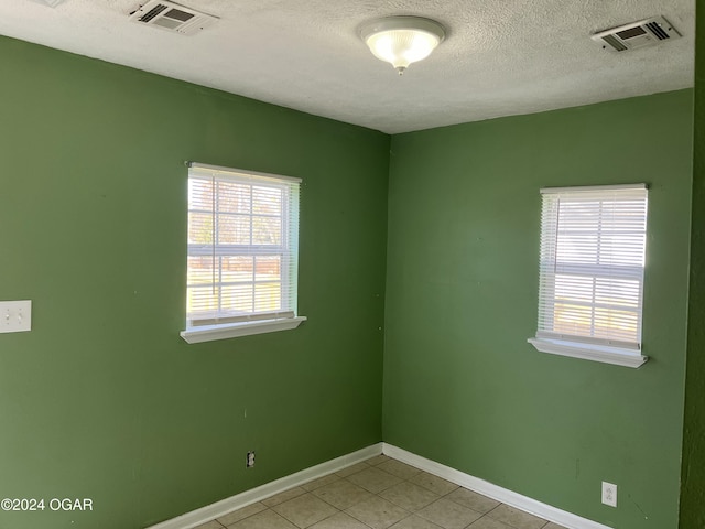 spare room featuring light tile patterned floors, baseboards, visible vents, and a textured ceiling