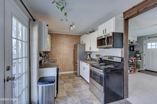 kitchen with dark countertops, brick wall, appliances with stainless steel finishes, white cabinetry, and a sink