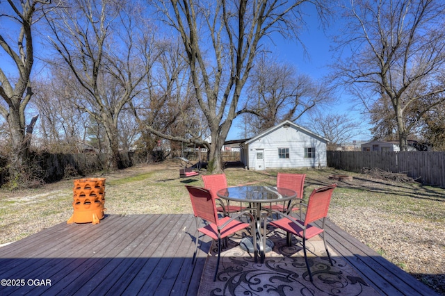 deck featuring outdoor dining area, a fenced backyard, an outdoor structure, and a lawn