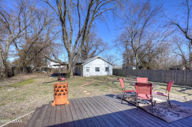 wooden terrace featuring outdoor dining space, an outdoor structure, a fenced backyard, and a yard