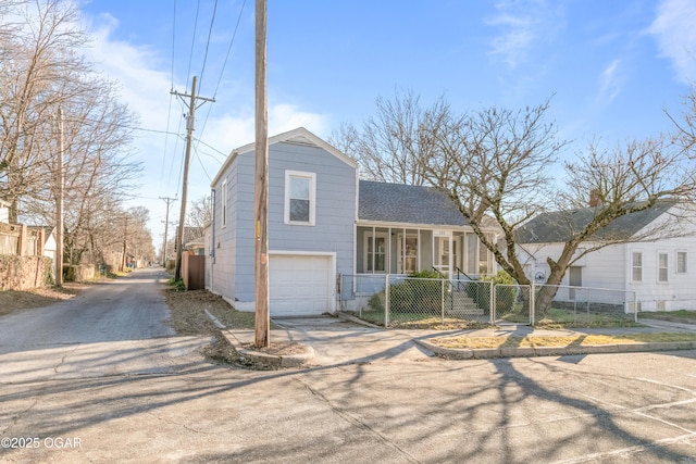 tri-level home featuring driveway, a fenced front yard, a garage, and roof with shingles