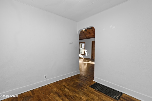 empty room featuring baseboards, visible vents, arched walkways, and dark wood-type flooring