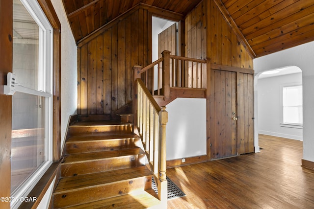 stairs with lofted ceiling, wooden walls, and wood finished floors