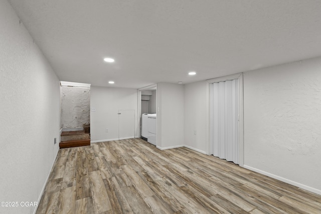 finished below grade area with a textured wall, stairway, wood finished floors, washer / dryer, and baseboards