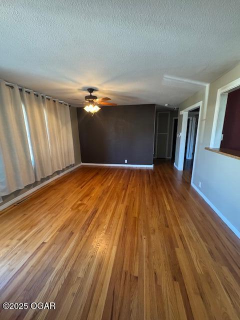 unfurnished living room with a textured ceiling, wood finished floors, a ceiling fan, and baseboards