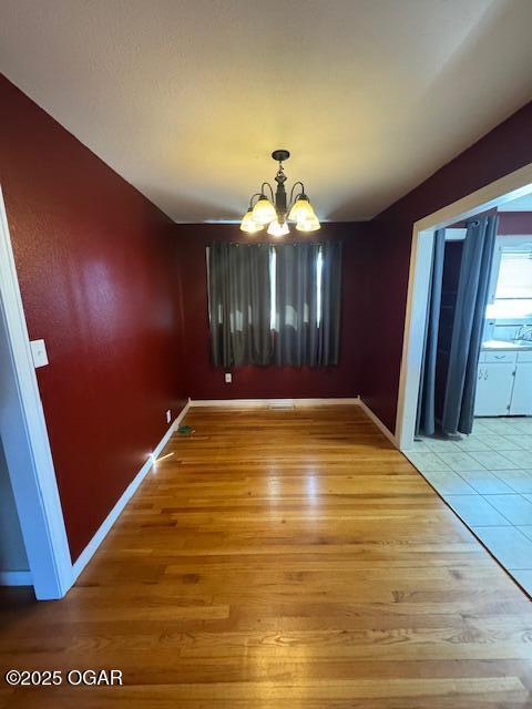 unfurnished dining area with a notable chandelier, baseboards, and wood finished floors