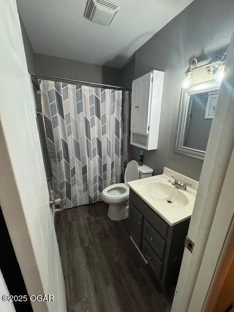 bathroom featuring curtained shower, toilet, wood finished floors, visible vents, and vanity