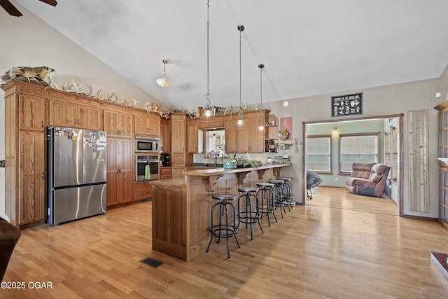 kitchen featuring visible vents, a breakfast bar, stainless steel appliances, a peninsula, and light wood finished floors