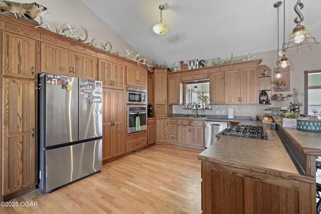 kitchen with lofted ceiling, light wood-style flooring, a peninsula, appliances with stainless steel finishes, and decorative light fixtures