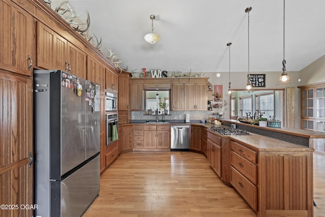 kitchen with a sink, light wood-style floors, appliances with stainless steel finishes, a peninsula, and lofted ceiling