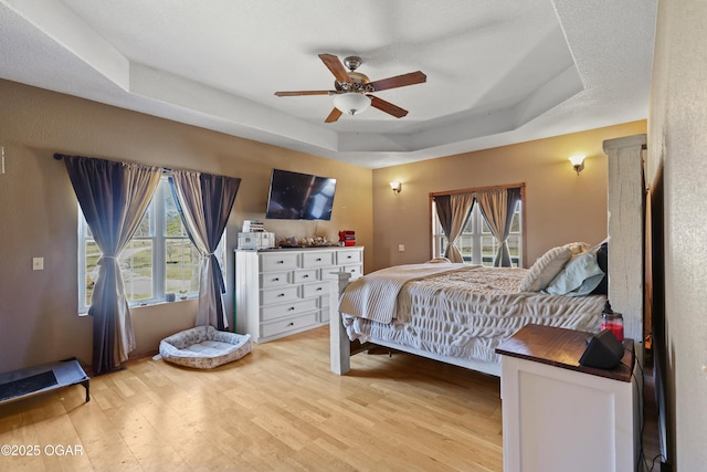 bedroom featuring a tray ceiling, light wood-style floors, and ceiling fan