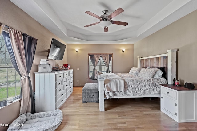 bedroom featuring a ceiling fan, a raised ceiling, and light wood-style floors