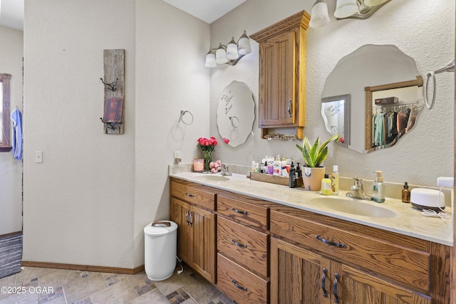 bathroom featuring double vanity, a textured wall, baseboards, and a sink