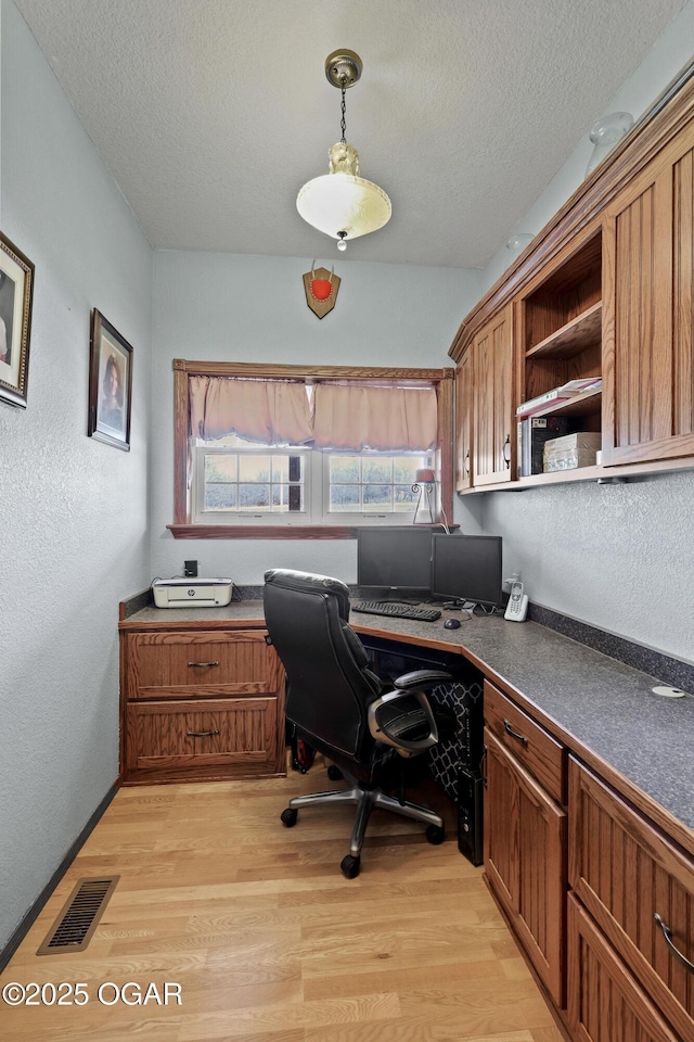 office featuring light wood-type flooring, visible vents, a textured ceiling, and built in desk