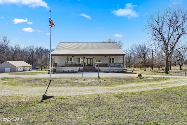 view of front of home with covered porch, driveway, metal roof, and a detached garage